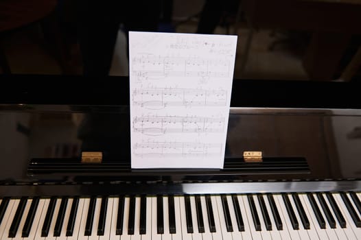 Still life of old vintage black piano with ebony and ivory keys and white paper sheet with musical notes of classic melody or composition. Classic luxury chord instrument,