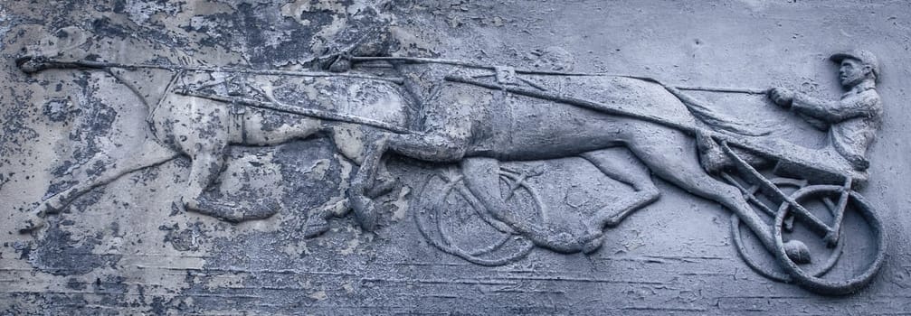 Close up metal relief with jockey and horses concept photo. Metal panel with ornament and horse rider figure. Part of antique old door photography. High quality picture