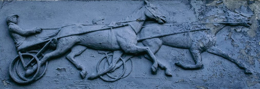 Close up metal bas-relief with jockey and horses concept photo. Metal panel with ornament and horse rider figure. Part of antique old door photography. High quality picture