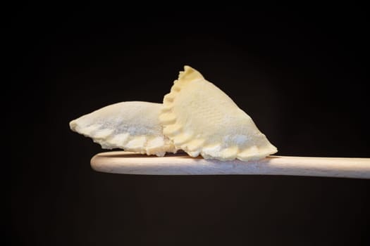 Raw dumplings with filling inside, Ukrainian cuisine. Raw dumplings for freezing on a wooden spoon isolated on a black background. Home kitchen.