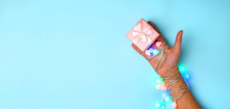 Hands with gift box on blue background composition, present. Flat lay with copy space.