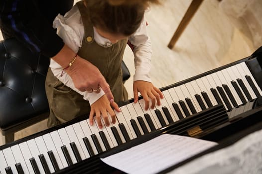 Closeup top view of child hand with fingers touching piano keys under the guidance of a musician pianist teacher explaining piano lesson