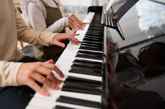 Close-up of the hands of two kids, boy and girl playing music on grand piano. Kids fingers on ebony and ivory keys. Music lesson