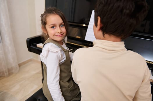 Handsome kids pianists playing grand piano, touching the black and white keys with his fingers to create the rhythm of the melody, smiling looking at the camera. People. Culture. Arts. Education