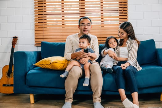 A happy family with kids finds relaxation and togetherness watching TV movies on the sofa in their modern living room. The father mother son and daughter share smiles laughter and fun.