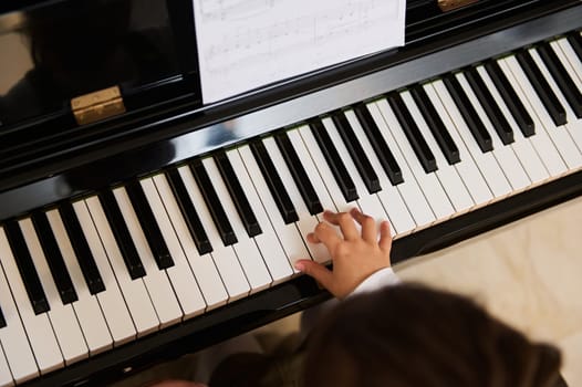 View from above of children hands on piano keyboard, touching white and black keys while playing music on grand piano. Chord instrument. Music lesson. Arts. Culture. Hobbies and entertainment