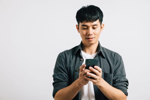 A happy Asian teenager types a text message on his smart mobile phone, enjoying online communication. Studio portrait isolated on white background, with copy space.