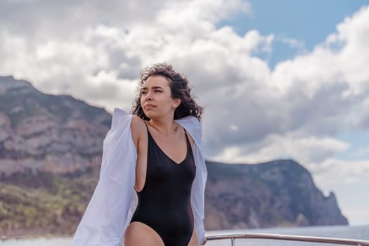 Woman on a yacht. Happy model in a swimsuit posing on a yacht against a blue sky with clouds and mountains.