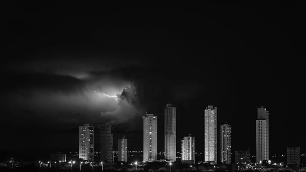 Night cityscape with towering skyscrapers forming a barrier against a dark electric storm with lightning and heavy clouds. Space for text and questions.