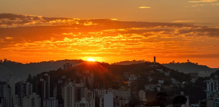 As the sun rises over the mountain at dawn, it creates an orange sky above the city, which waits in darkness for the morning light.