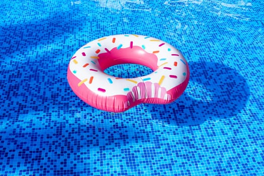 A rubber bitten donut with caramel sprinkles floats in a clean pool.