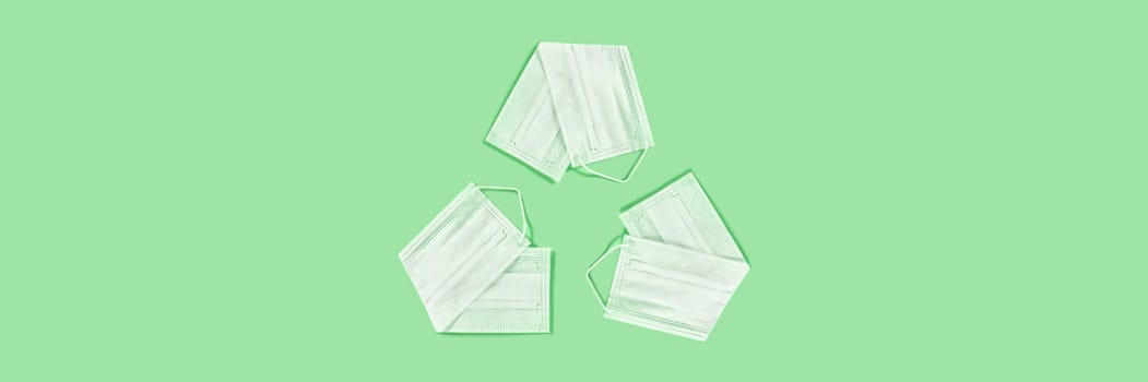 The universal recycling symbol made from the medical masks on green background.