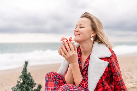 Lady in plaid shirt holding a gift in his hands enjoys beach with Christmas tree. Coastal area. Christmas, New Year holidays concep.