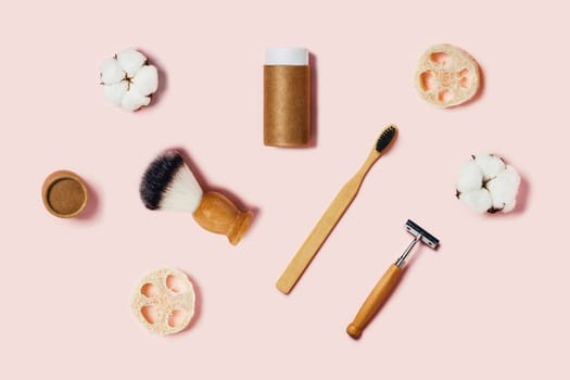 Bathroom accessories on pink background. Natural bamboo toothbrushes, sponges, cotton flowers, shaving brush, razor. Flat lay, top view.