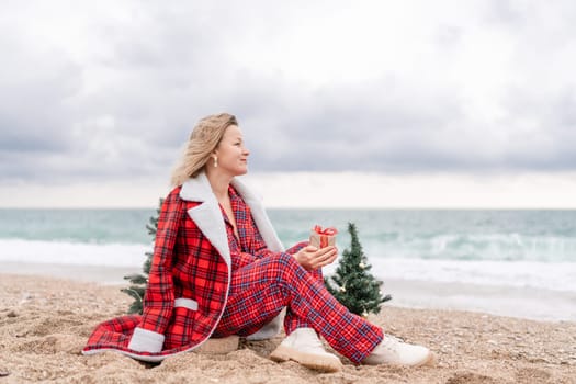 Lady in plaid shirt holding a gift in his hands enjoys beach with Christmas tree. Coastal area. Christmas, New Year holidays concep.