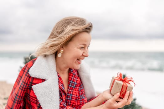 Lady in plaid shirt holding a gift in his hands enjoys beach with Christmas tree. Coastal area. Christmas, New Year holidays concep.