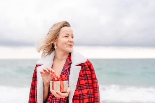 Lady in plaid shirt holding a gift in his hands enjoys beach. Coastal area. Christmas, New Year holidays concep.