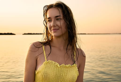 Close-up portrait of a young woman in a yellow dress at sunrise against the background of the sea. Woman walks on the seashore