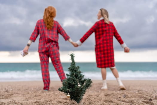 Sea two Lady in plaid shirt with a christmas tree in her hands enjoys beach. Coastal area. Christmas, New Year holidays concep.