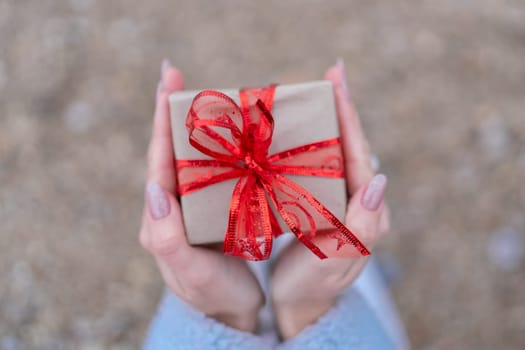 Hand holding wrapped gift with red bow. Sea Beach backdrop. The hand holding the gift is the main focus of the image, emphasizing the act of giving and receiving