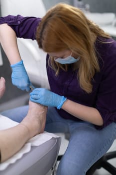 Close-up of a woman's feet having a pedicure performed. A podiatrist cuts a client's toenails with a sharp tool. Relaxing with a beautician. Undergoing a cosmetic treatment.