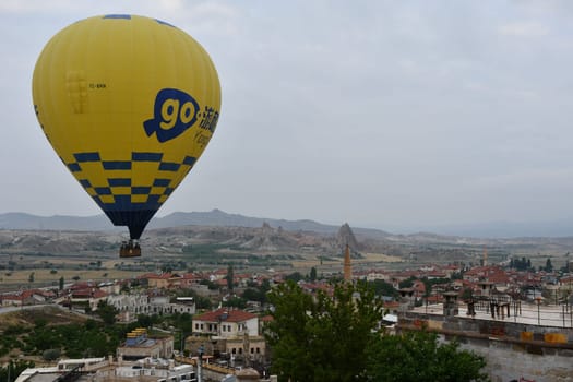 Yellow hot air balloon with the inscription go over the village of Cavusin in Cappadocia, Turkey