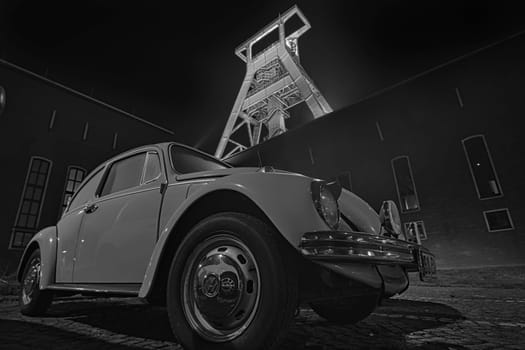 Low-angle grayscale of an old VW beetle in front of an old mining conveyor in Bochum, Germany