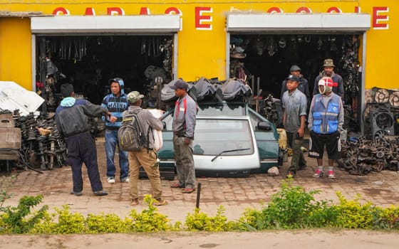 Antananarivo, Madagascar - May 07, 2019: Local Malagasy men standing and chatting in front of garage workshop with various cars components. Recycled vehicle parts are often sold by the road like this