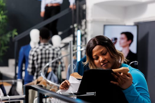 African american customer checking shirt fabric, shopping for elegant present for husband in modern boutique. Stylish woman looking at racks full with fashionable merchandise. Fashion concept