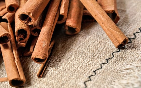 Closeup detail - Heap of cinnamon bark sticks on linen tablecloth. 