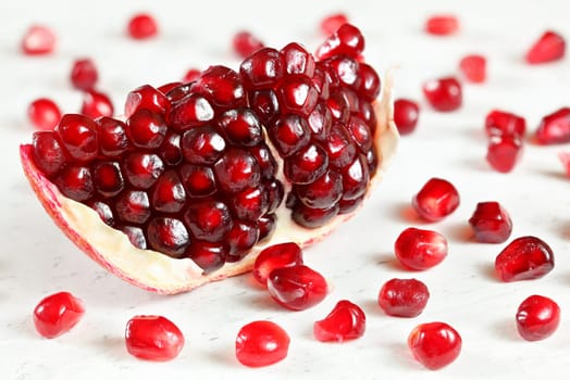 Pomegranate fruit halved, berries looking like red gems scattered on white board