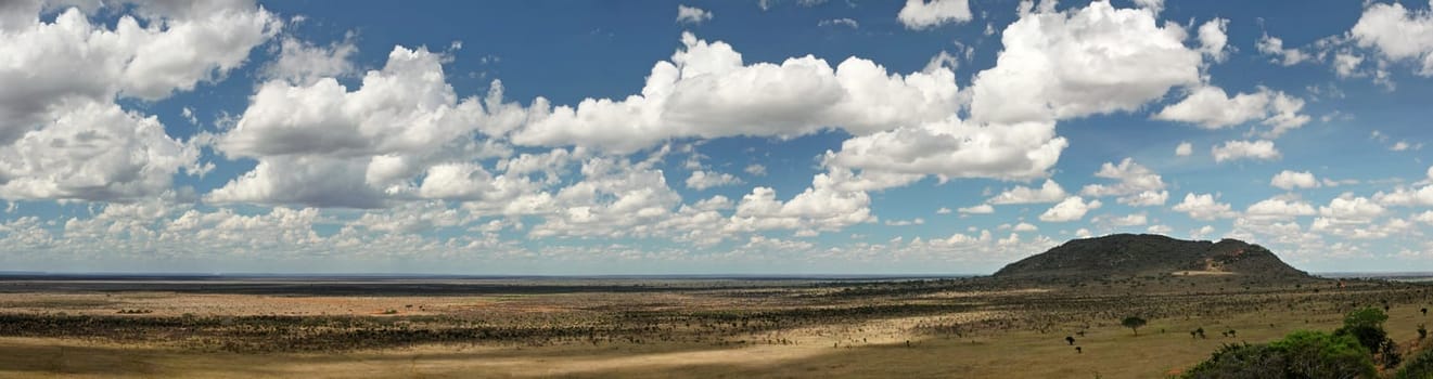 Wide panorama banner of Tsavo East national park, dramatic clouds over small hill in distance