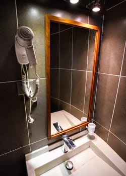 Modern bathroom in hotel room, white porcelain wash basin, mirror and hair dryer on the wall. Wide angle photo