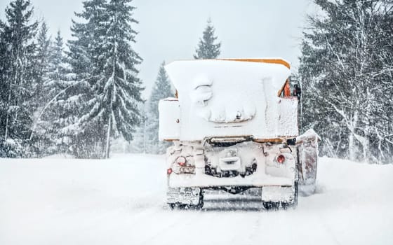 Orange highway maintenance truck removing snow from completely white road during blizzard snowstorm, trees on both sides of road