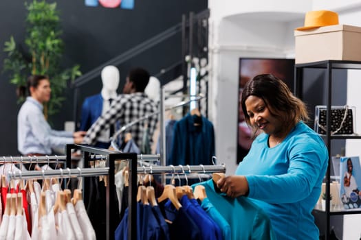 African american customer discount shirt material in modern boutique, shopping for fashionable merchandise. Shopaholic woman buying casual wear clothes in clothing store. Fashion concept