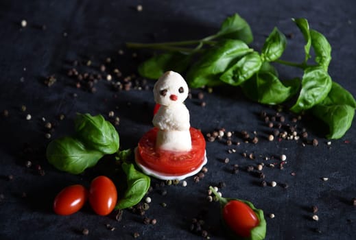 woman making funny still life with a festive appetizer of an edible mozzarella snowman with cherry tomatoes, cheese and basil, cheerful serving for the Christmas table, high quality photo