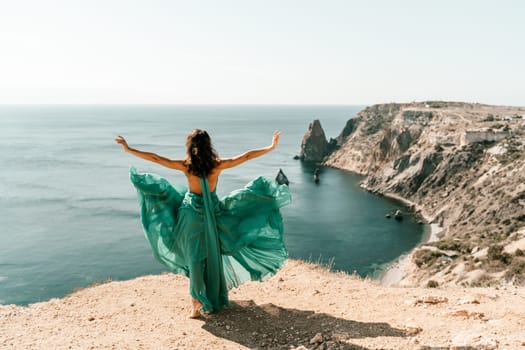 Woman green dress sea. Female dancer posing on a rocky outcrop high above the sea. Girl on the nature on blue sky background. Fashion photo