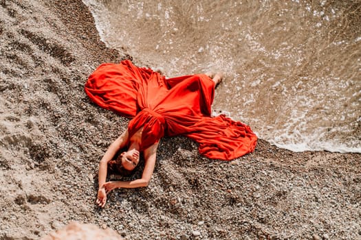 Woman red dress sea. Female dancer in a long red dress posing on a beach with rocks on sunny day.