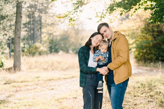 Mom and dad hugging while holding their little daughter in their arms in the park. High quality photo