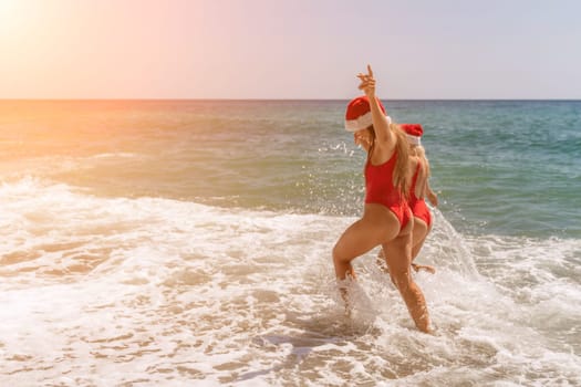 Women in Santa Claus hats run into the sea dressed in red swimsuits. Celebrating the New Year in a hot country.