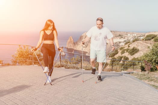 Happy Middle aged couple or friends practicing nordic walking in park near sea. Mature couple with trekking poles walking, practicing Nordic walking outdoors. Aging youthfully and sport concept.