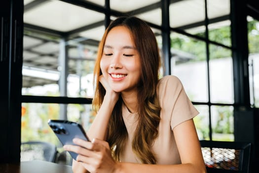 Beautiful Asian female has transfer money financial internet banking on mobile phone, young woman using smart phone for shopping online at cafe coffee shop near windows in the morning