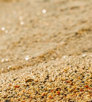 A background of sand, small pebbles and flowing waves on the sea beach. Summer vacation and coastal nature concept