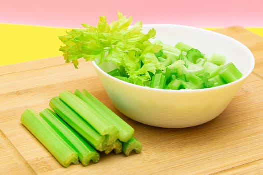 Fresh Chopped Celery Slices in White Bowl with Celery Sticks on Bamboo Cutting Board. Vegan and Vegetarian Culture. Raw Food. Healthy Diet with Negative Calorie Content