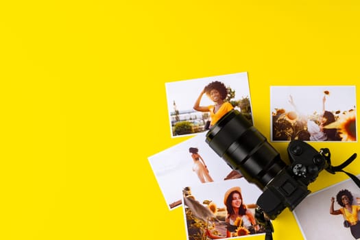 Photo camera with colorful printer photos on yellow background, top view