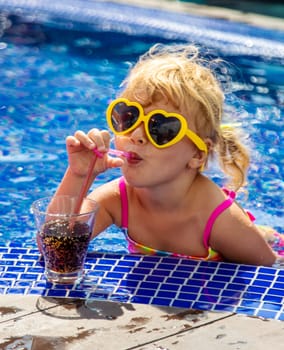 A child near the pool in sunglasses drinks a cocktail. Selective focus. Kid.