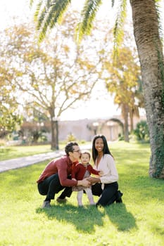 Dad kisses the temple of a little girl sitting next to mom in a sunny park. High quality photo