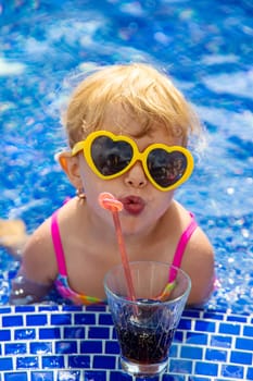 A child near the pool in sunglasses drinks a cocktail. Selective focus. Kid.