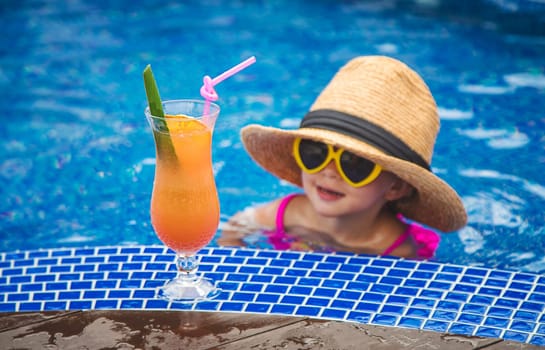 A child in the pool drinks a cocktail. Selective focus. Kid.