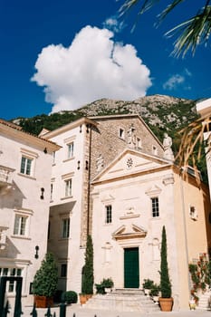 Church of St. Mark the Apostle among ancient houses and green trees in flowerpots. Perast, Montenegro. High quality photo